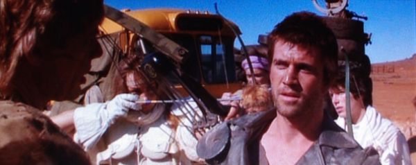 Mad Max 2: Max (Mel Gibson) entre dans la communauté aux côtés de Pappagallo (Michael Preston) et d'une guerrière (Virginia Hey)
